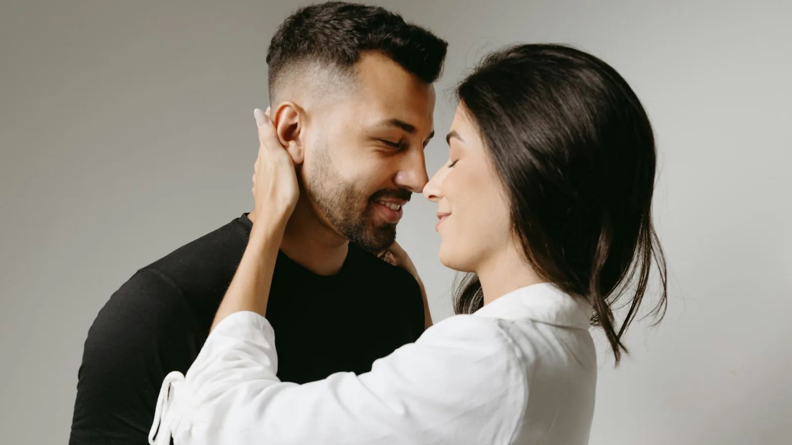 Zwei Menschen stehen mit den Gesichtern nah beieinander; eine Hand liegt seitlich am Kopf der anderen Person.