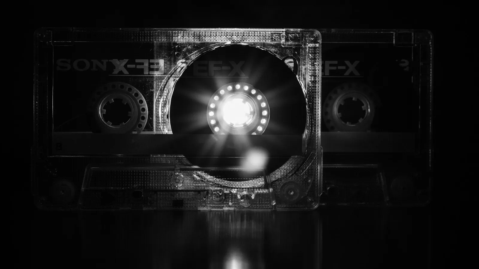 Eine transparente Audiokassette mit hellem Lichtschein in ihrer Mitte vor schwarzem Hintergrund.