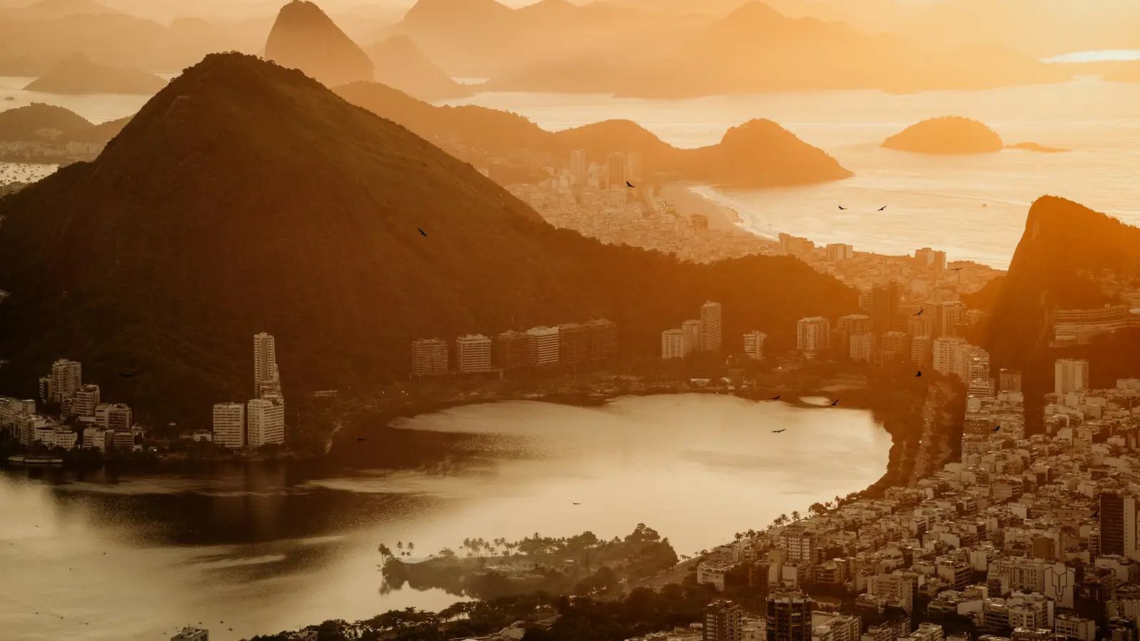 Stadt und bewaldete Berge zwischen einer Lagune und dem Meer im goldenen Abendlicht.